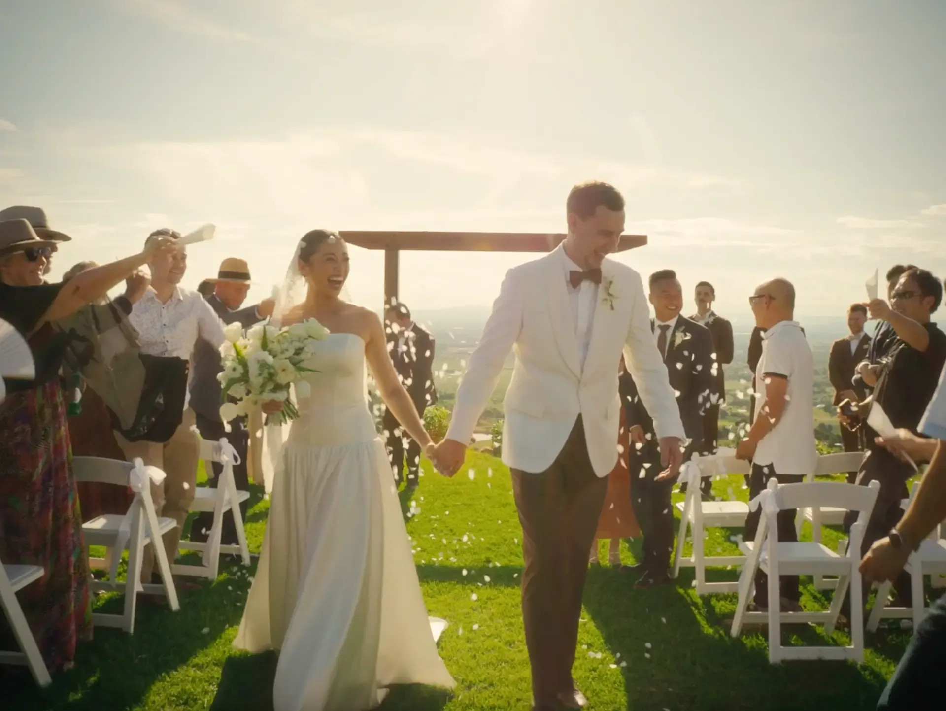 Couple walking back down the aisle through falling petals at an outdoor hilltop ceremony